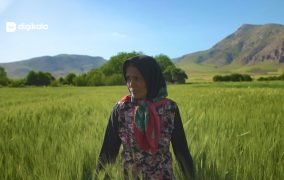 یکی از زنان روستای هرسین کرمانشاه در حال راه رفتن در زمین کشاورزی