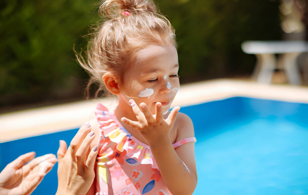 یک دختربچه در کنار استخر که به صورت خود ضدآفتاب می‌زند