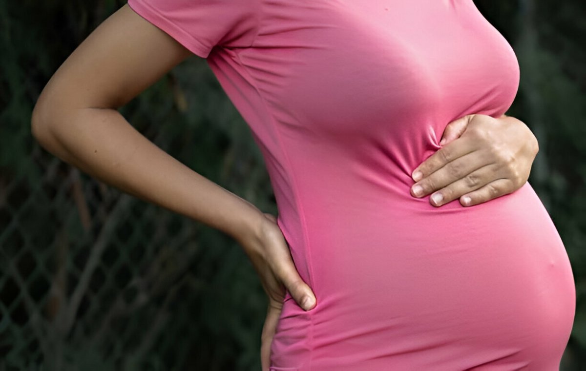  زن باردار یک دست را روی شکم و دیگری را روی کمر قرار داده است