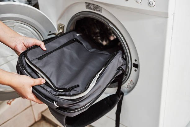 Washing and cleaning backpack in washing machine. Loading dirty school backpack into washing machine. Clean backpack. Washing school bag. Person places backpack in wash machine