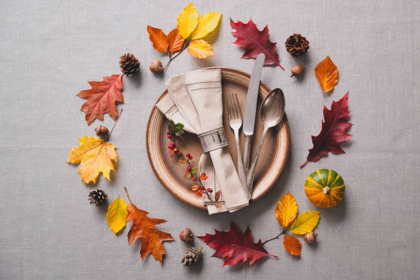 Thanksgiving autumn table setting with cutlery and arrangement of colorful fall leaves and pumpkin