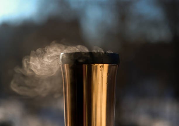 The copper thermos cup or the travel mug. The movement of steam. Dark photo.