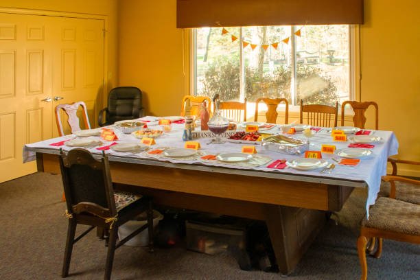 A table with a white tablecloth and a number of plates and utensils. The table is set for a Thanksgiving dinner