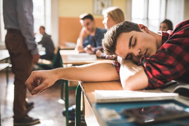 Bored male high school student sleeping during the lecture in the classroom.