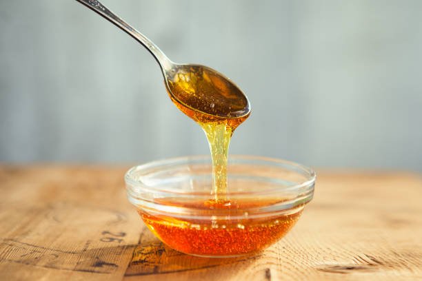 Honey dripping from spoon in the cup in golden sunlight