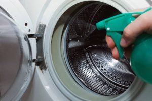 Dirty washing machine being sprayed with a cleaning products.